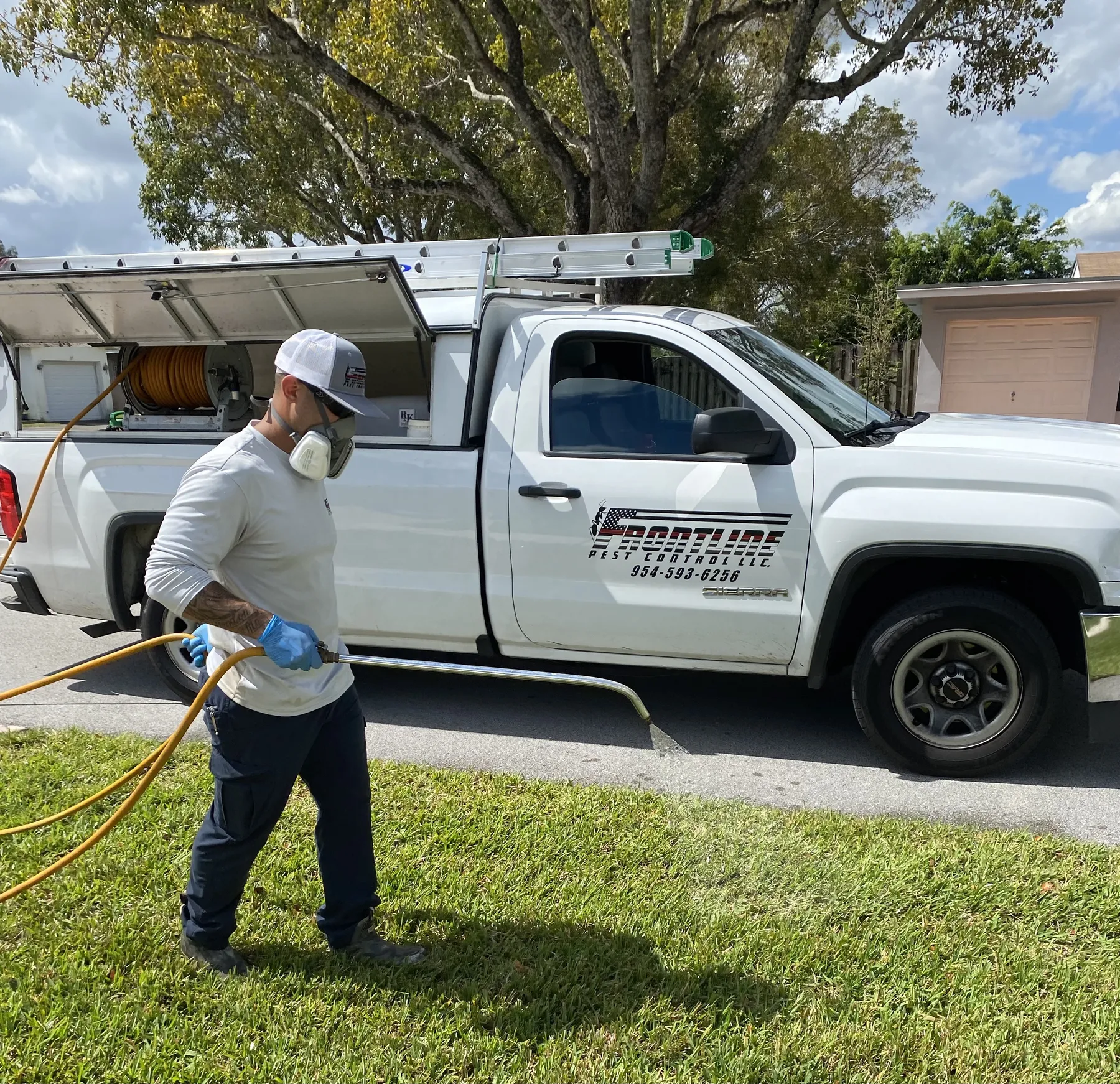Frontline Pest Control technician pulling a spray hose beside a branded service truck